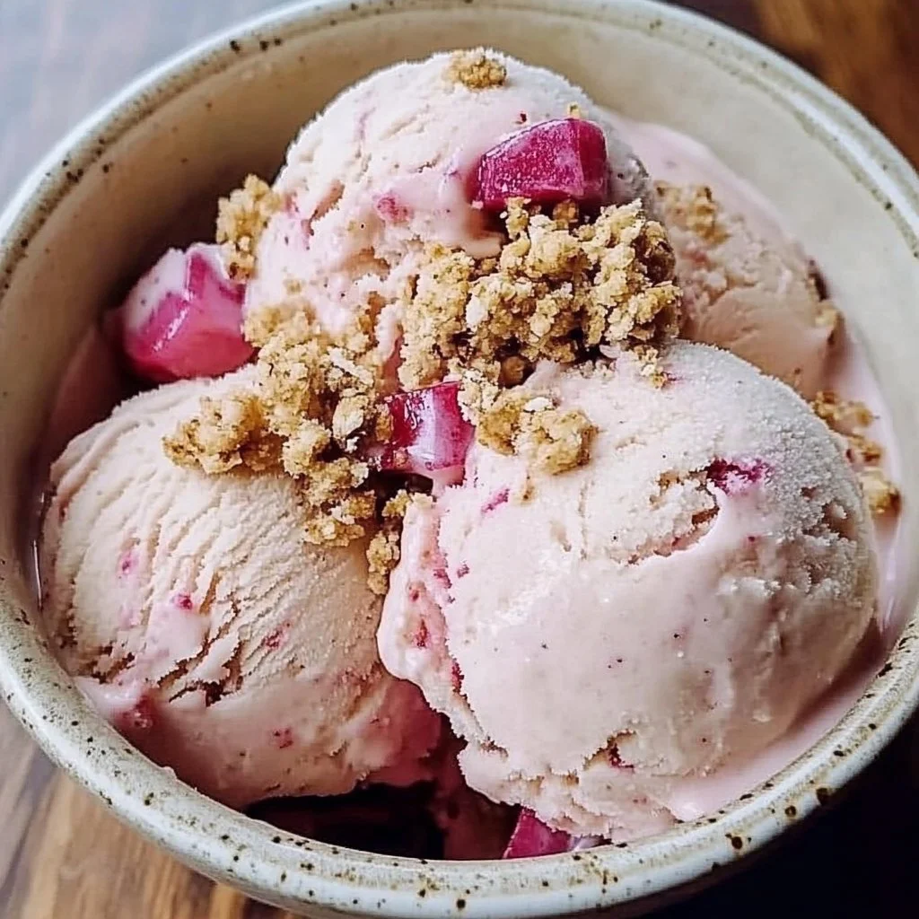 Bowl of rhubarb crumble ice cream topped with crumble pieces and mint leaves.